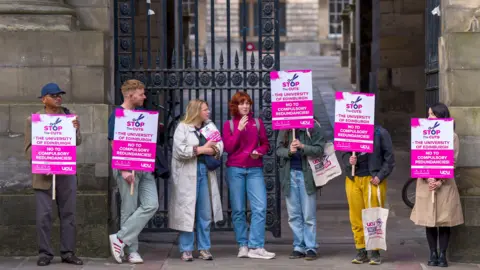 Pa Media Photo muestra a miembros de la UCU en la Universidad de Edimburgo, que participaron en una huelga en septiembre de 2025, en una disputa sobre los planes para reducir £ 140 millones del presupuesto universitario. La foto muestra a siete personas afuera de un edificio cerrado que tiene carteles rosas que dicen
